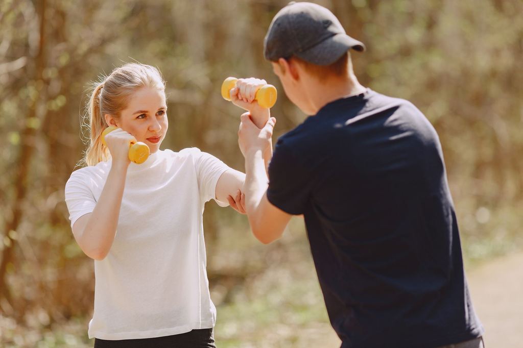 Personal trainer orientando uma aluna com halteres em um parque